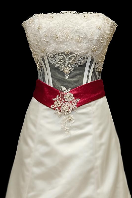 Długa wytworna suknia ślubna z koronkowym gorsetem, delikatnymi rękawkami i czerwonymi dodatkami.